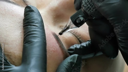Master in gloves does tattoo of eyebrows close-up photo
