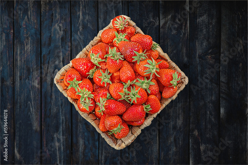 Strawberries in a basket on a wooden table, top view