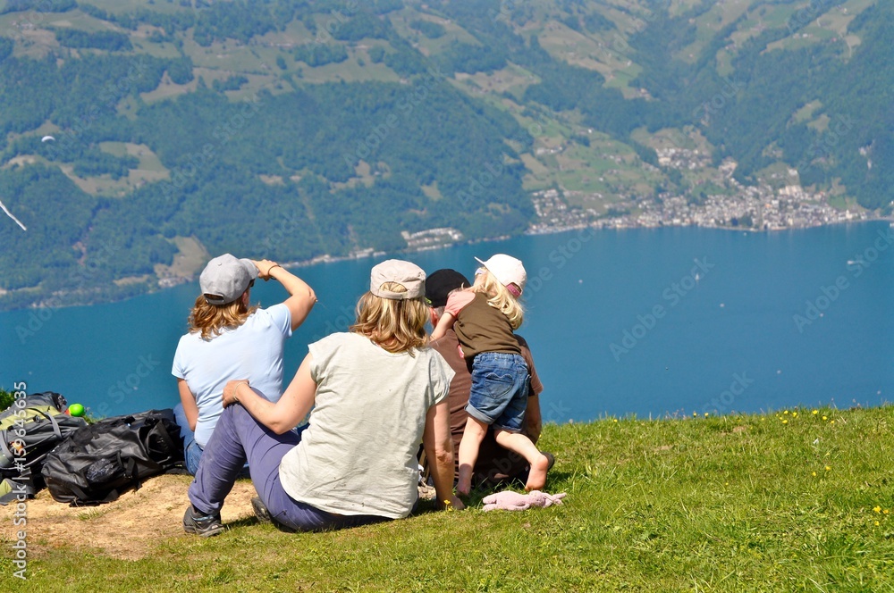 Wanderer / Familie sitzt nach Wanderung auf der Wiese einer Schweizer Alp und geniesst die Aussicht auf den See / Vierwaldstättersee Wanderer / Familie sitzt nach Wanderung auf der Wiese einer Schweizer Alp und geniesst die Aussicht auf den See / Vierwaldstättersee