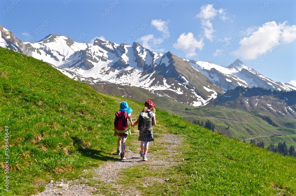 Kinder wandern Hand in Hand in den Schweizer Alpen. Im Hintergrund Schneeberge