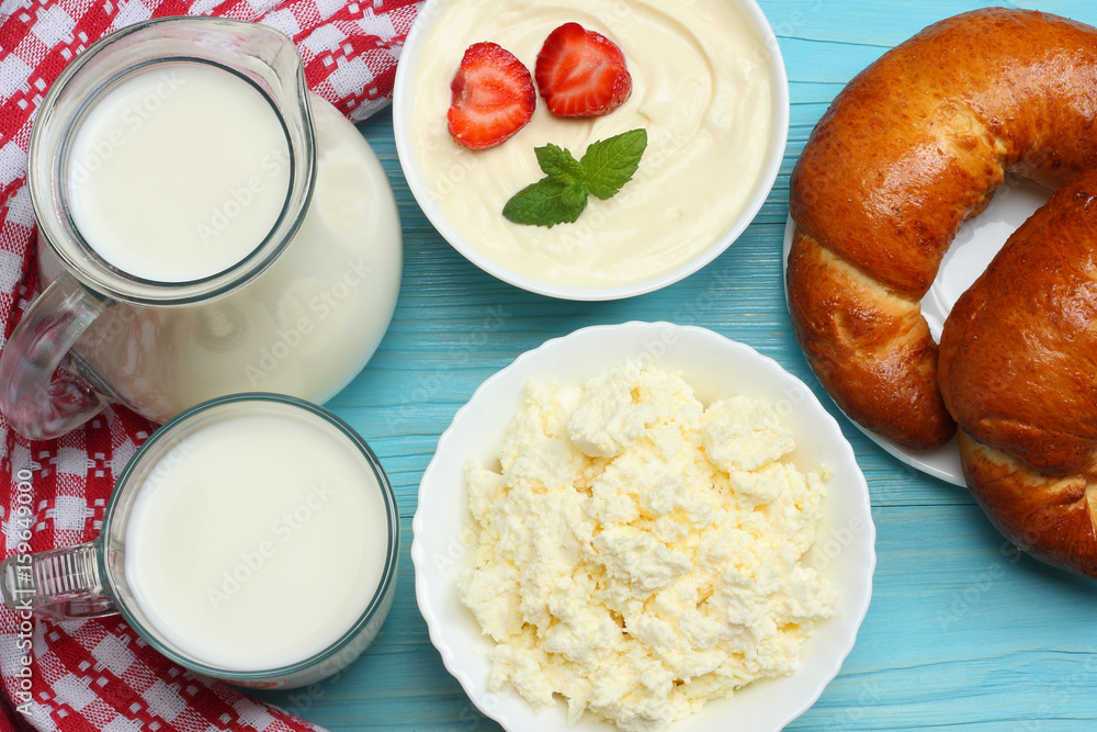 Milk background. Glass jug pitcher of fresh milk with glass, sour cream, cottage cheese and croissant on blue wooden background. Top view with copy space. Milk background. Glass jug pitcher of fresh milk with glass, sour cream, cottage cheese and croissant on blue wooden background. Top view with copy space.