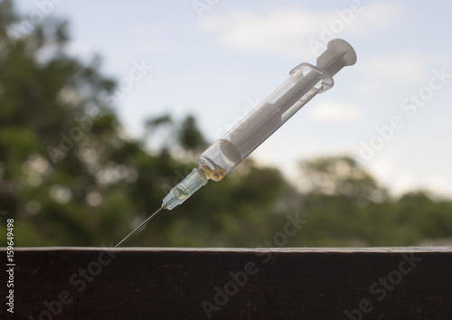 Syringe sticking out on the board against the background of trees and sky