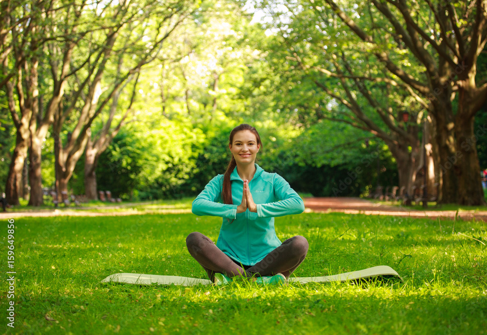 Smiling young woman in summer park doing yoga
