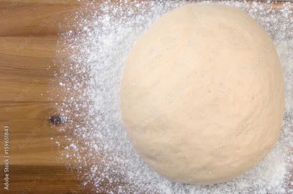 Ball a dough and white flour on a wooden cutting board. Top view, close up. Ball a dough and white flour on a wooden cutting board. Top view, close up.