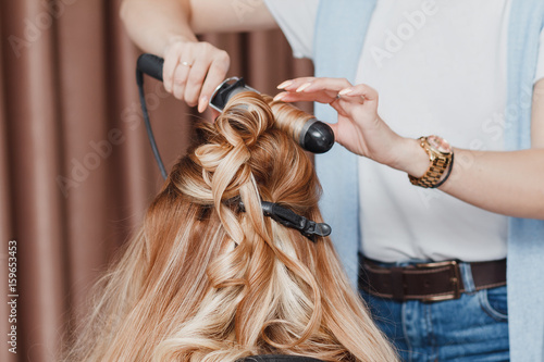 Woman hairdresser making hairstyle in beauty salon using iron curler