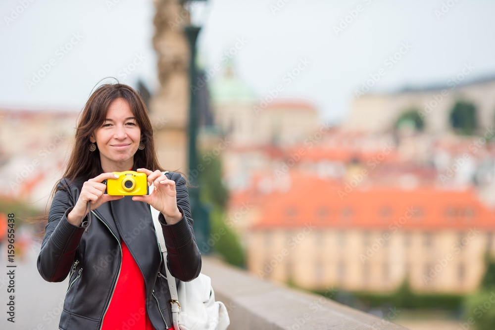 Happy young woman in european city on the famous bridge. Caucasian tourist take a photo by her camera in Prague Happy young woman in european city on the famous bridge. Caucasian tourist take a photo by her camera in Prague