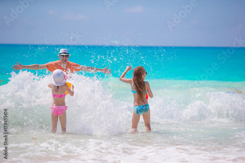 Little girls and happy dad having fun on the seashore swimming and running
