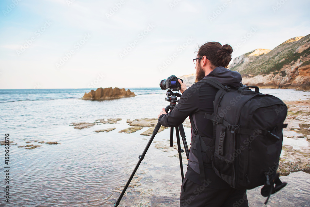 Young stylish photographer making photos of sea with the camera on a tripod