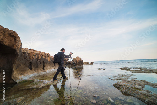 Young stylish photographer making photos of sea with the camera on a tripod © bodiaphoto