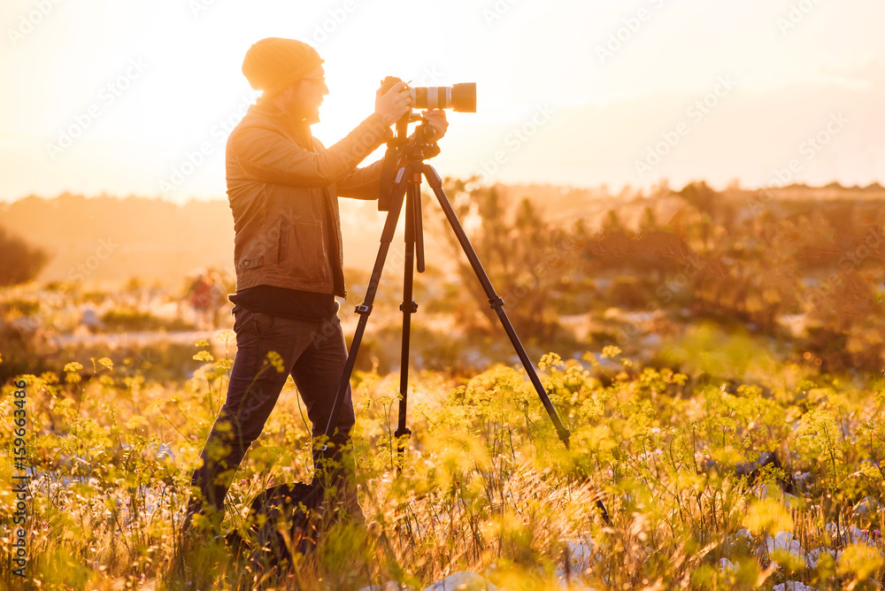 Portrait of photographer making photos with camera on tripod at sunset