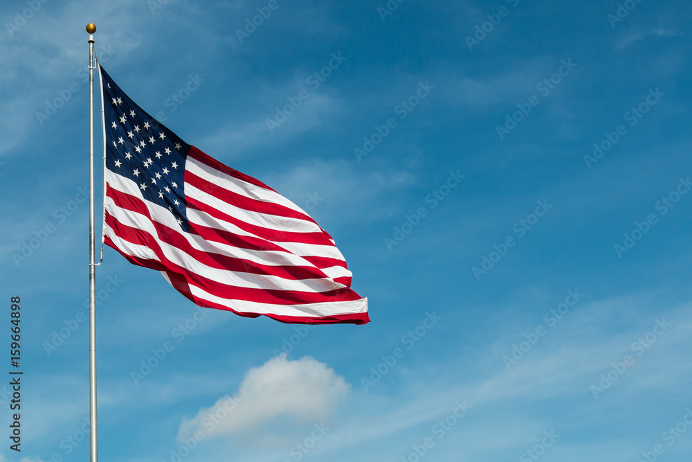 Fototapeta premium American Flag against the backdrop of a blue sky and clouds. 