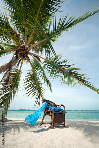 wicker chair in the shade of palm tree on beach