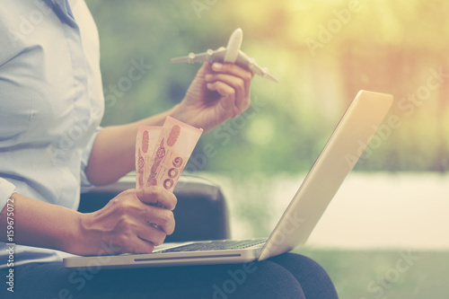 Young business woman using laptop computer and holding airplane with money. travel concept