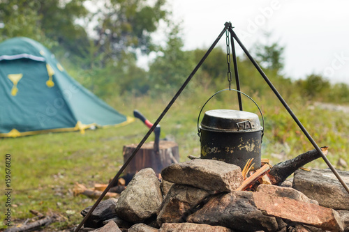 Cauldrons over burning campfire with camping tent in background on Baikal