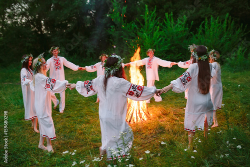 Midsummer. Young people in Slavic clothes circle dance around a bonfire in the forest. photo