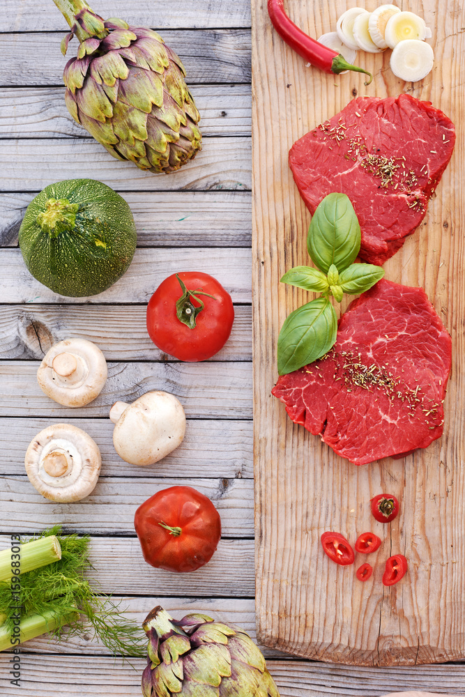 Top view of raw beef steaks on wooden board with fresh vegetables and champignons ready to be grilled. Top view of raw beef steaks on wooden board with fresh vegetables and champignons ready to be grilled.