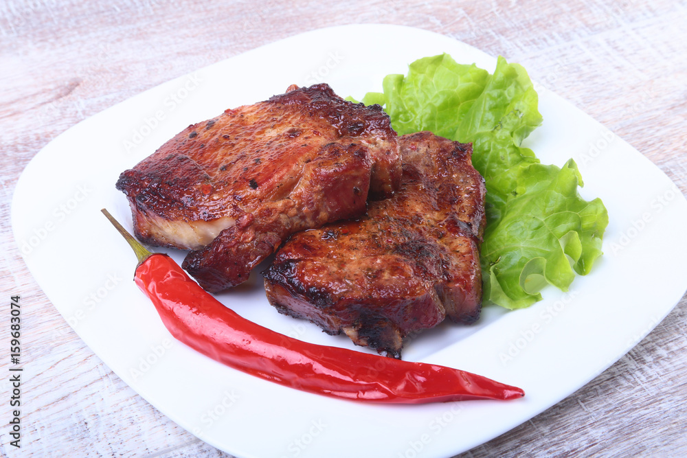 Steak of grilled meat and chili pepper with tomato, lettuce leaves on white plate. Steak of grilled meat and chili pepper with tomato, lettuce leaves on white plate.