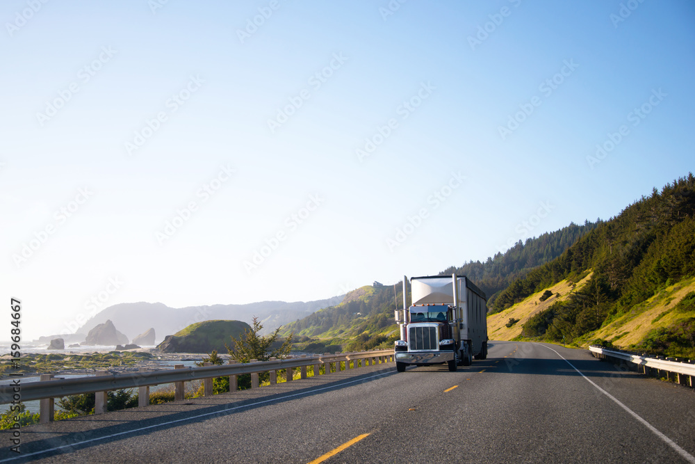 Dark classic semi truck with trailer driving on highway along the Pacific coast in Northwest