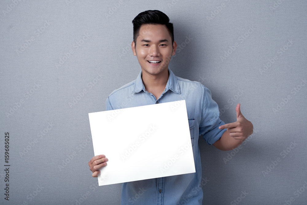 Waist-up portrait of smiling Asian man posing for photography while holding blank sheet of paper in hands, studio shot Waist-up portrait of smiling Asian man posing for photography while holding blank sheet of paper in hands, studio shot
