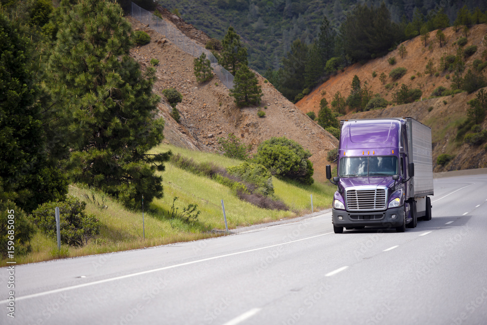 Lilac semi truck with aluminum trailer is moving along winding highway Lilac semi truck with aluminum trailer is moving along winding highway