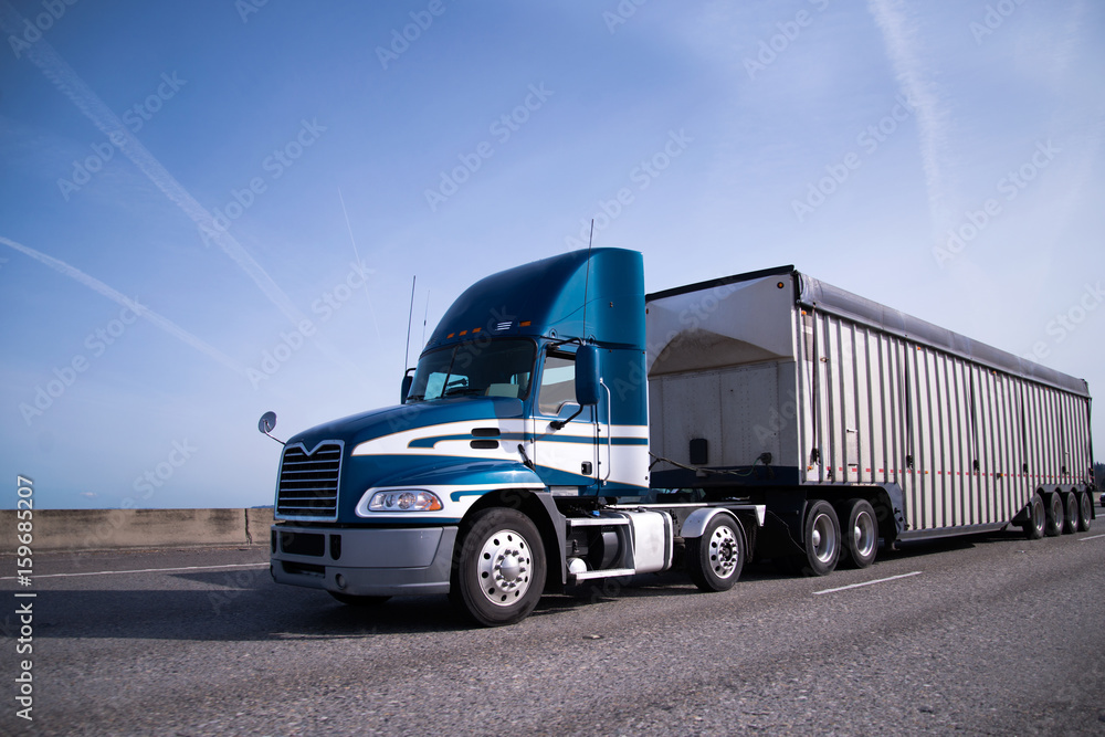 Modern blue semi truck with day cab and bulk trailer on interstate highway