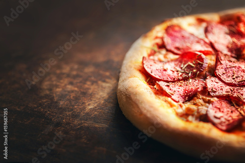 Pizza with pepperoni and salami on a rustic wooden table.