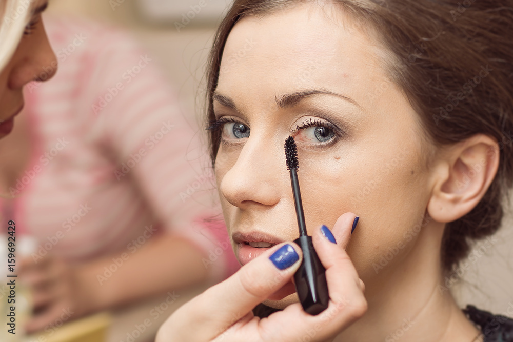 Make-up of a beautiful, young girl before the wedding ceremony. Very beautiful, sharpen eyes. The hand of the make-up artist and cosmetic brush is present. Glamour.