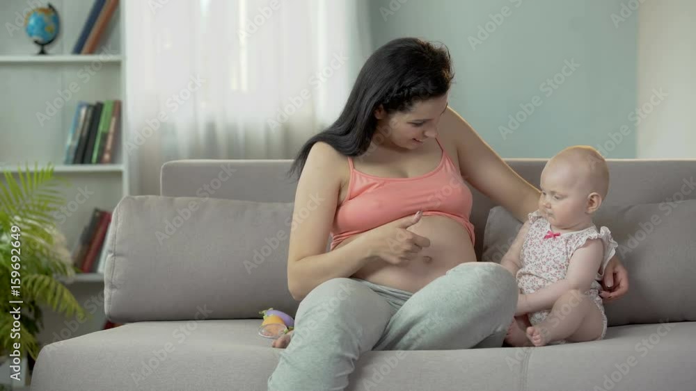 Woman enjoying pregnancy, touching her big belly and hugging cute baby girl Woman enjoying pregnancy, touching her big belly and hugging cute baby girl