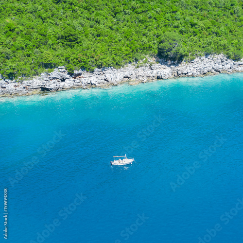 Man aboard a white boat in the sea near a green shore © watman