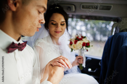 Wedding couple sitting inside modern cool car. Looking at each other's eyes. Close-up photo.
