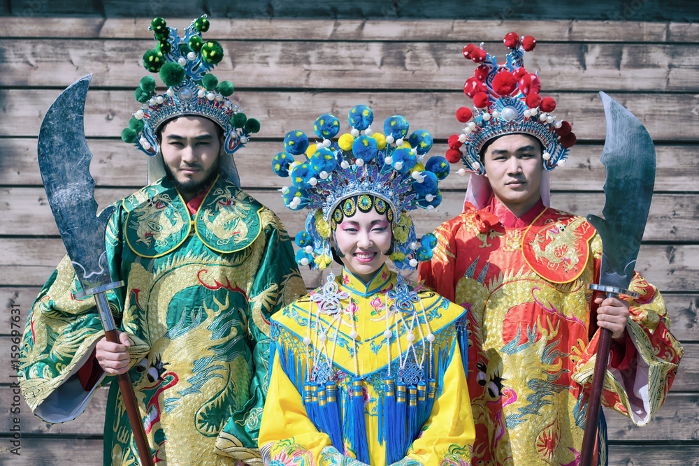 group of three asian people men and woman standing in a row and greeting outdoor in traditional chinese costumes