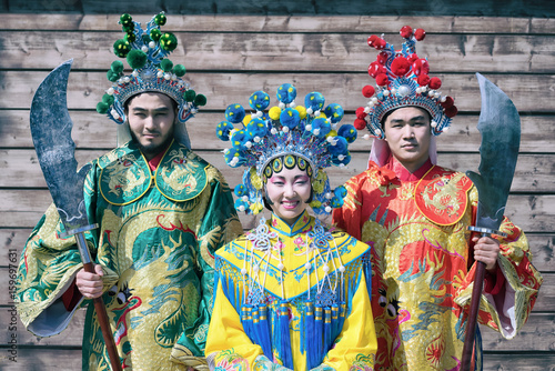 group of three asian people men and woman standing in a row and greeting outdoor in traditional chinese costumes