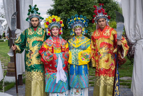 group of four asian people men and women standing in a row and greeting outdoor in traditional chinese costumes