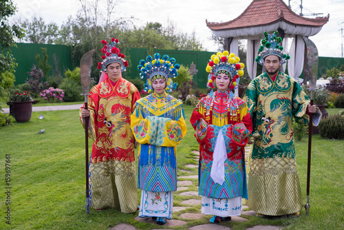 group of four asian people men and women standing in a row and greeting outdoor in traditional chinese costumes