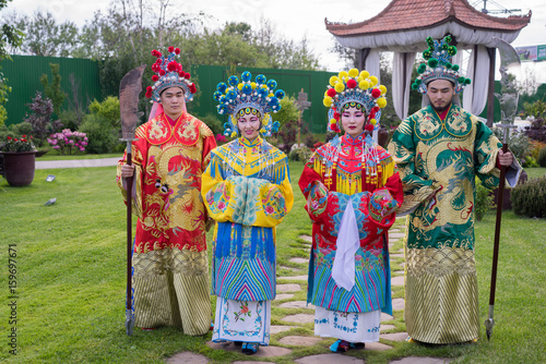 group of four asian people men and women standing in a row and greeting outdoor in traditional chinese costumes