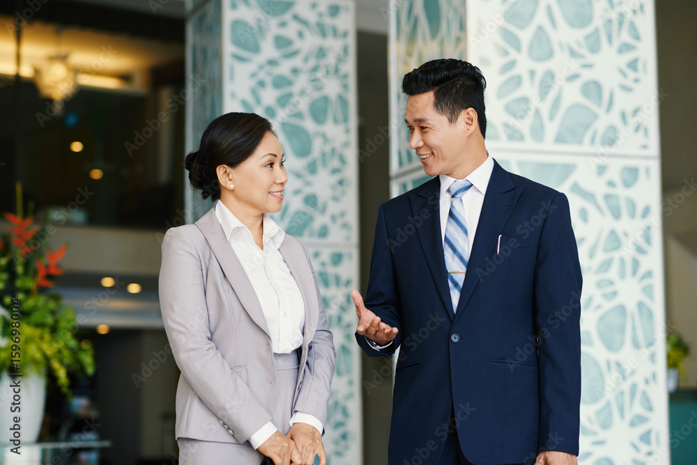 Group portrait of middle-aged Vietnamese coworkers having small talk while standing in office lobby and waiting for beginning of conference Group portrait of middle-aged Vietnamese coworkers having small talk while standing in office lobby and waiting for beginning of conference