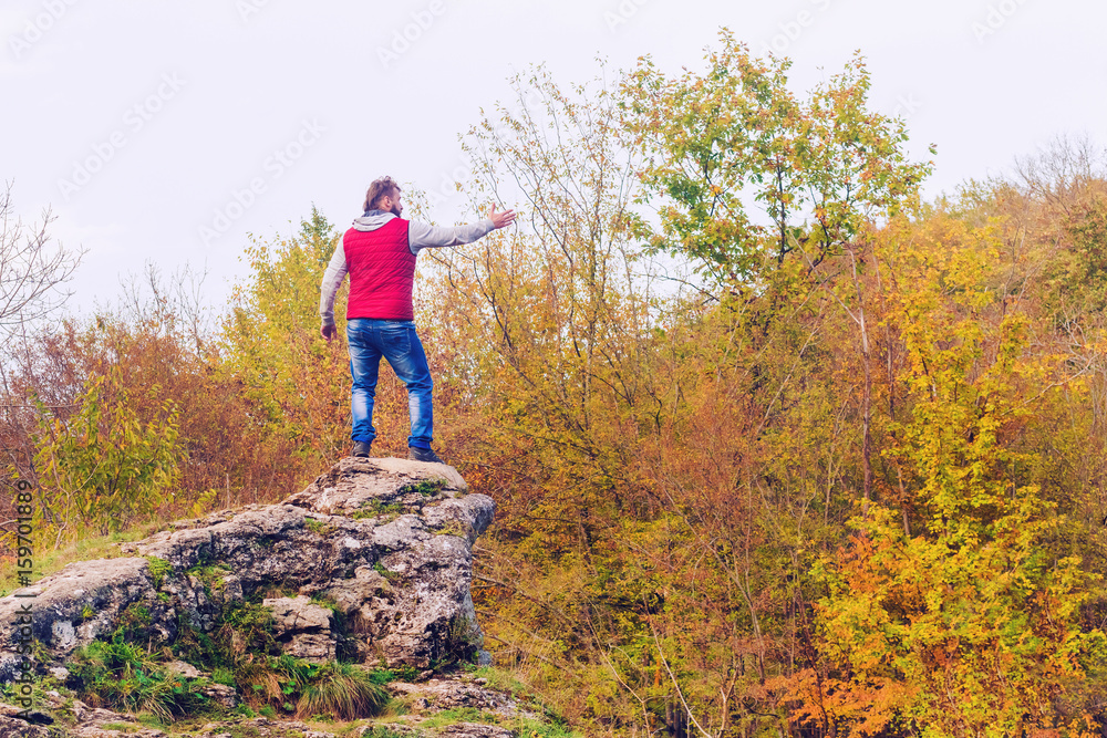 Man in a red vest standing on a rock and showing a hand forward