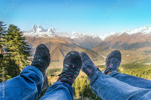 Male and female legs in sneakers and jeans on the background of mountains