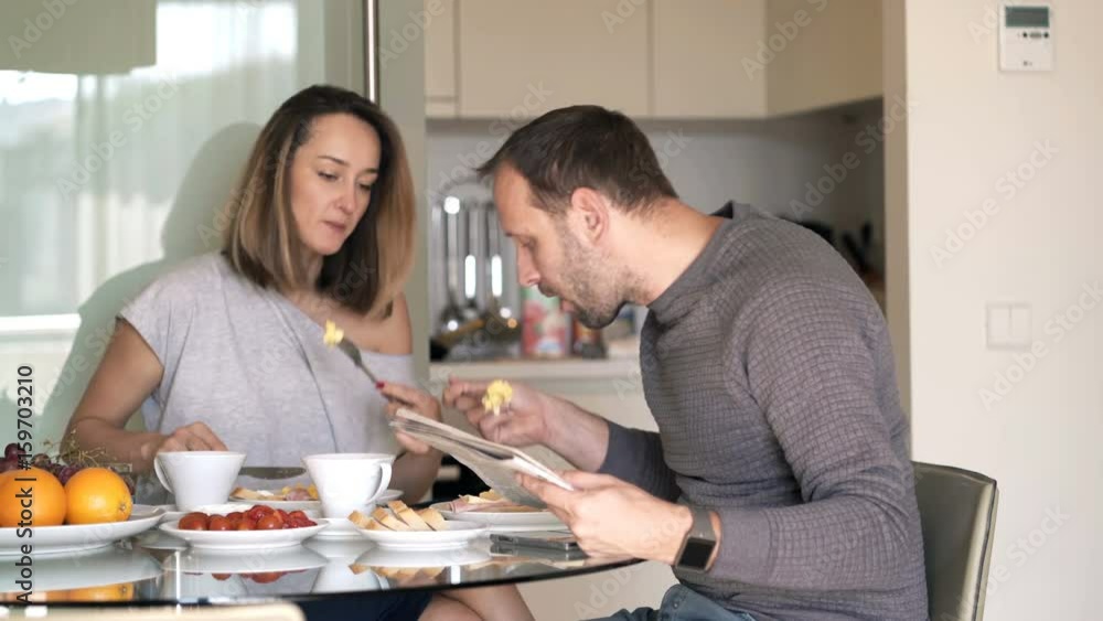 Young couple eating breakfast at home, man reading newspaper
Young couple eating breakfast at home, man reading newspaper