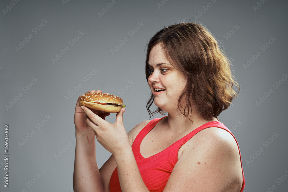 Hungry woman looking at a hamburger, woman with a hamburger on a gray background Hungry woman looking at a hamburger, woman with a hamburger on a gray background