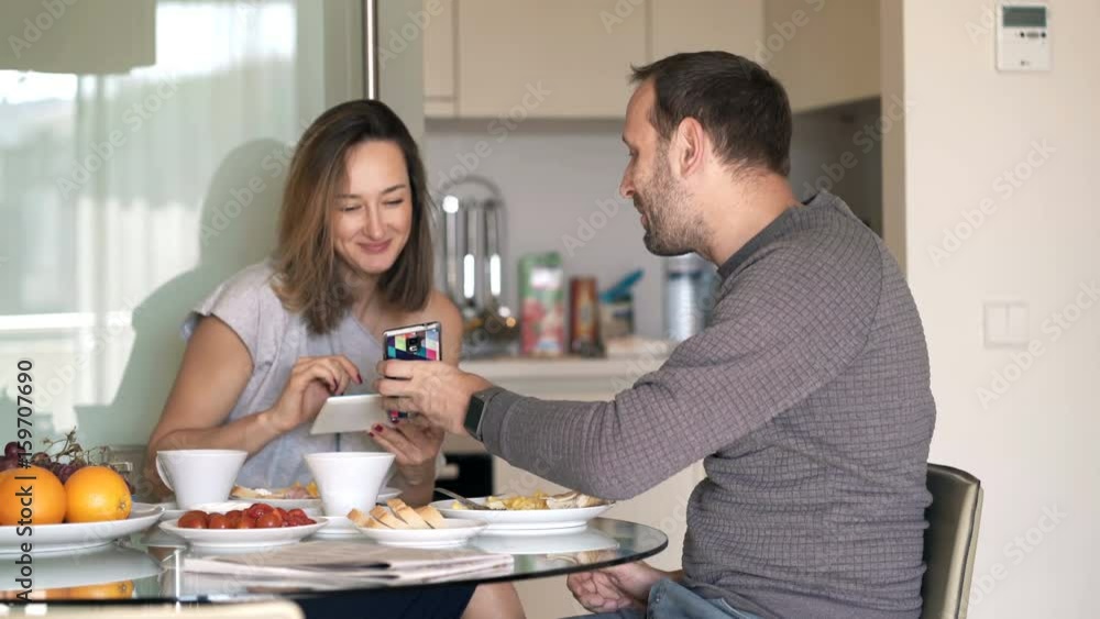 Couple with tablet computer and smartphone talking during breakfast at home Couple with tablet computer and smartphone talking during breakfast at home