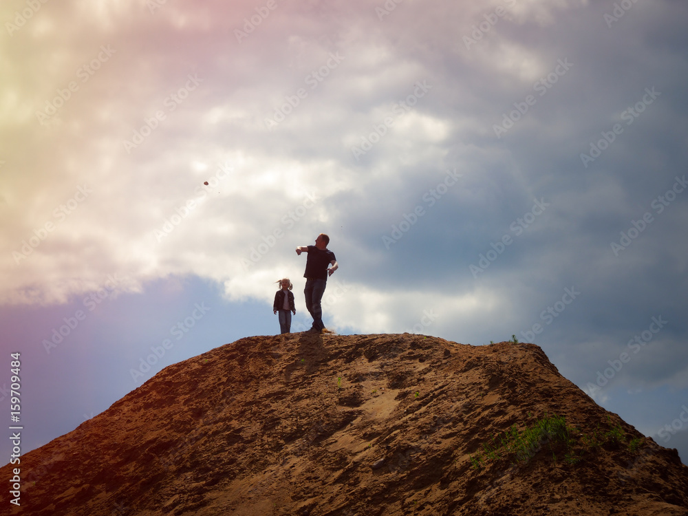 Father and child on the top of the mountain against the sky. Dad throws a stone down from a height