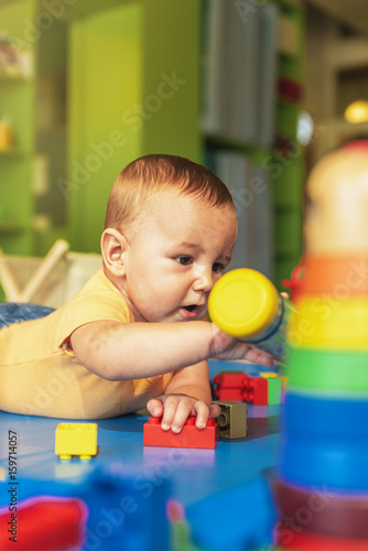 Happy baby playing with toy blocks in the kindergarten.