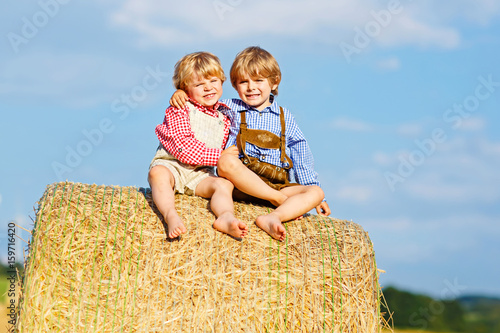 Two little kid boys, twins and siblings sitting on warm summer day on hay stack