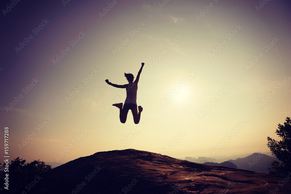 Young woman jumping on rocky mountain peak face the sunrise