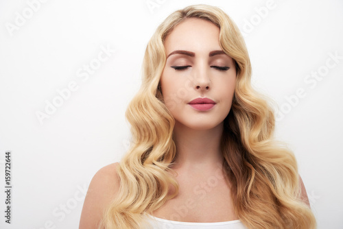 Portrait of beautiful young woman with wavy blond hair and eyes closed standing against white background