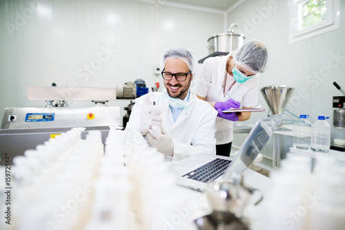 Young technologist making face care creams. Sitting in a cosmetic products factory with his female assistant.