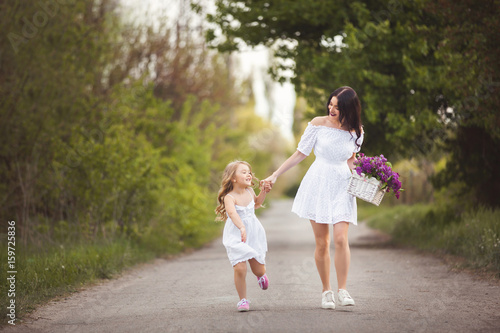 Young beautiful mother and little daughter having fun together. Pretty mom and cute girl outdoors. Cheerful family together rinning taking by the hand