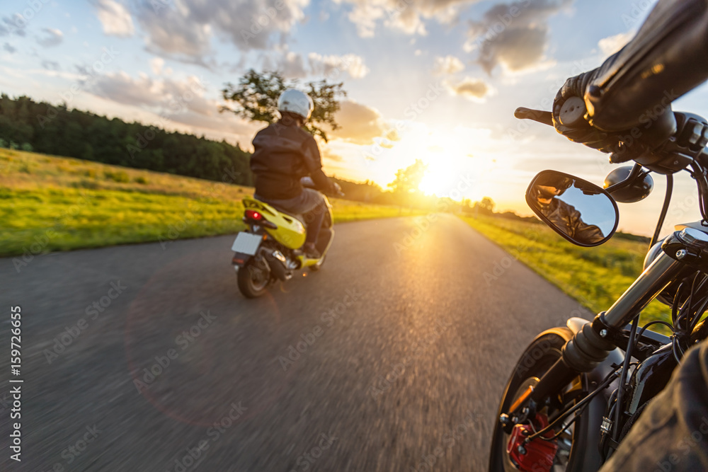 Fototapeta premium Motocykliści jadący w kierunku pięknego światła zachodzącego słońca na pustej asfaltowej autostradzie.