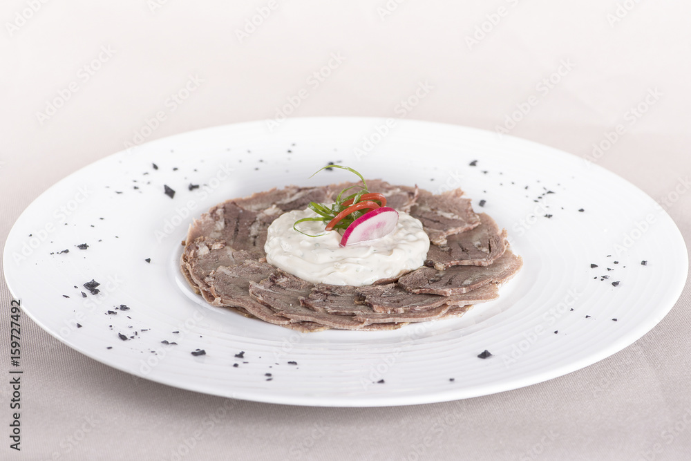 Beef carpaccio with mayonnaise, decorated with herbs, placed on white plate, light background, isolated